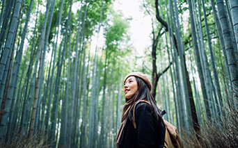 woman walking in the forest looking up at the trees